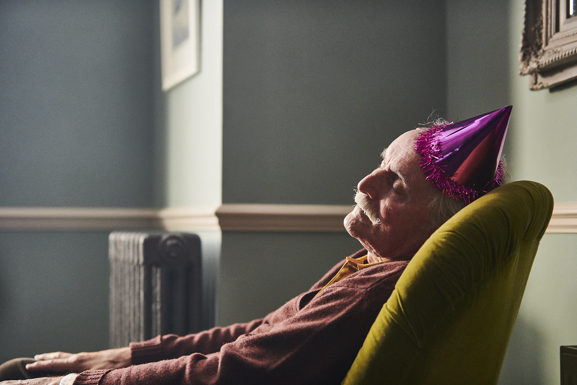 An elderly man having a nap on an armchair