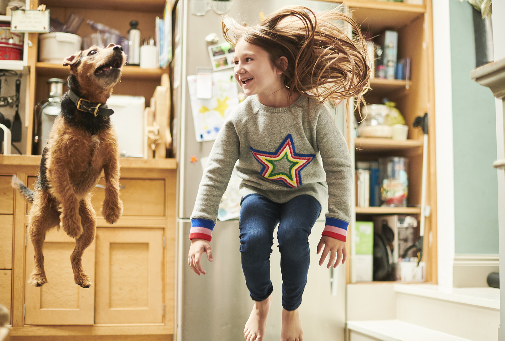 A young girl and her dog jumping in their kitchen