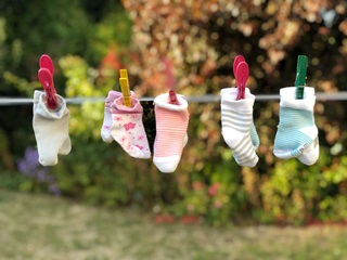 Five pairs of baby socks hanging on a washing line in a garden