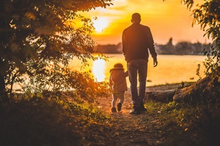 Father and child walking towards the sunset on a lake