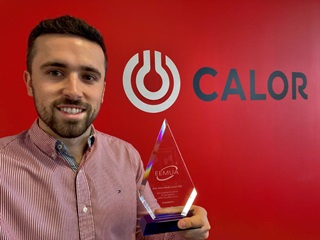 Calor Graduate, Morgan Tiley, holding his Engineering award. Calor logo on red wall in the background