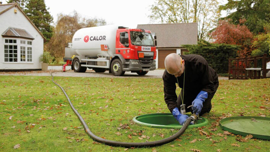 Calor engineer filling up an underground tank. Gas truck and house in the background.