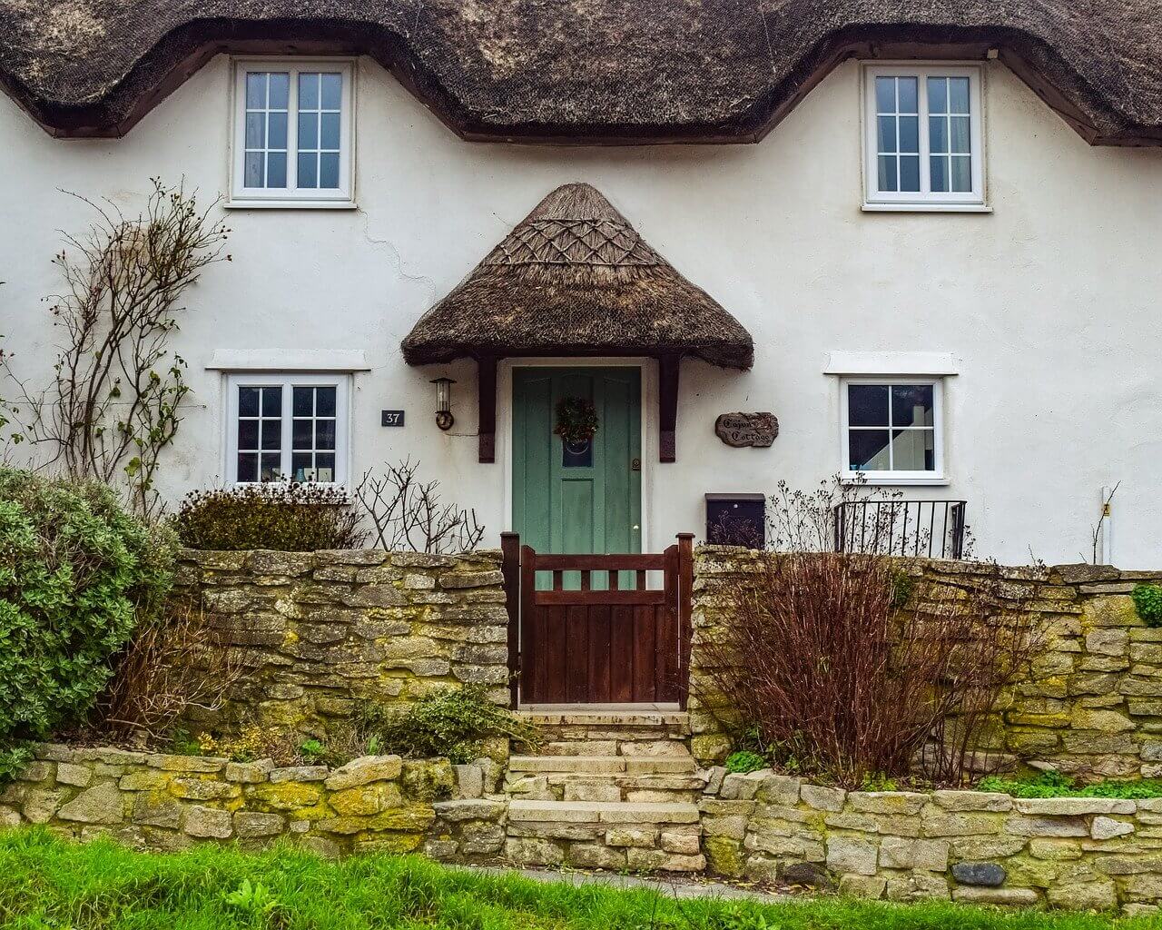 White countryside cottage with a thatched rood and green door.