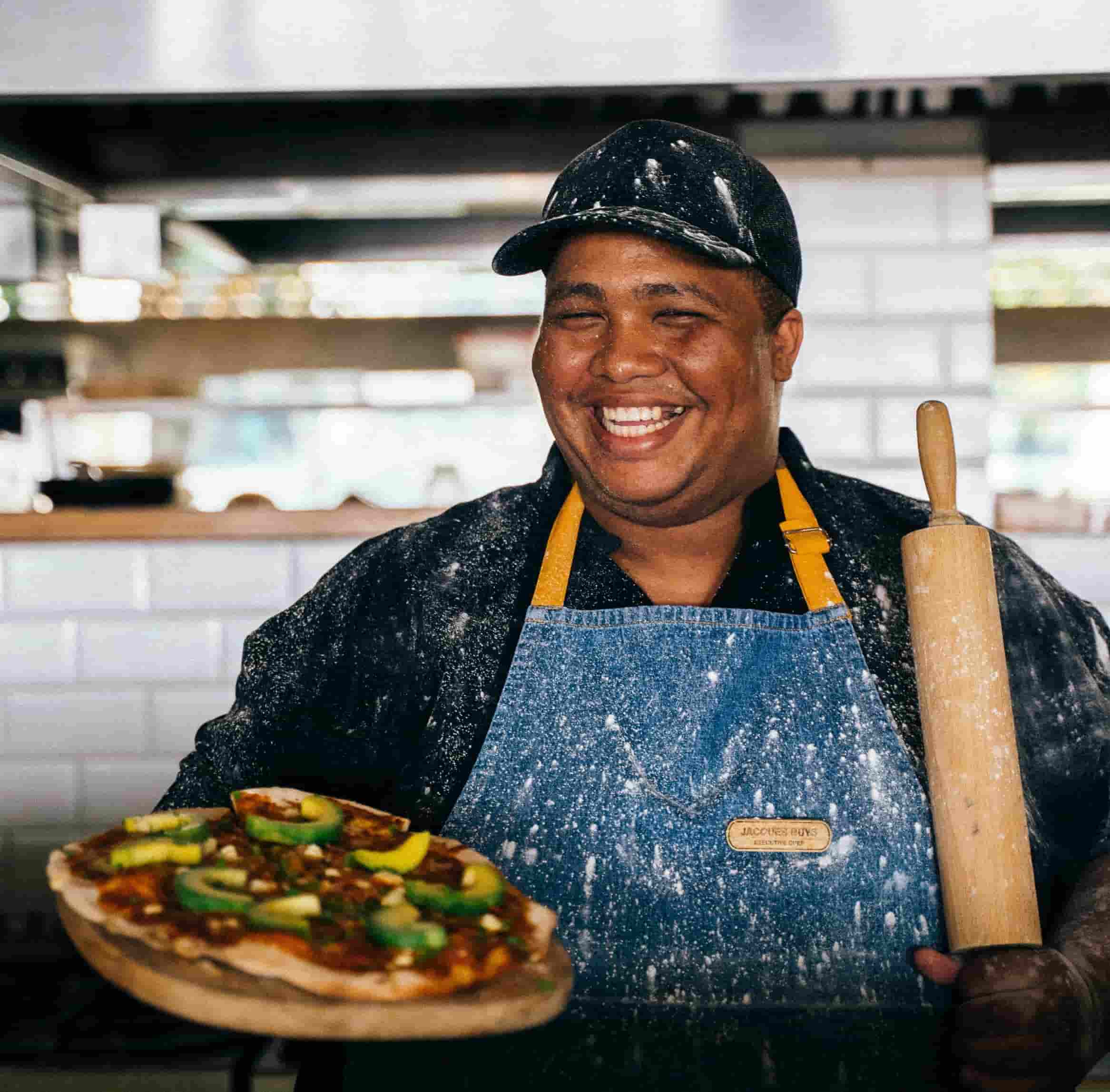 Male chef with blue apron holding a pizza and a rolling pin