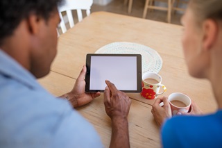 A couple sitting at their dining table, looking at their tablet   