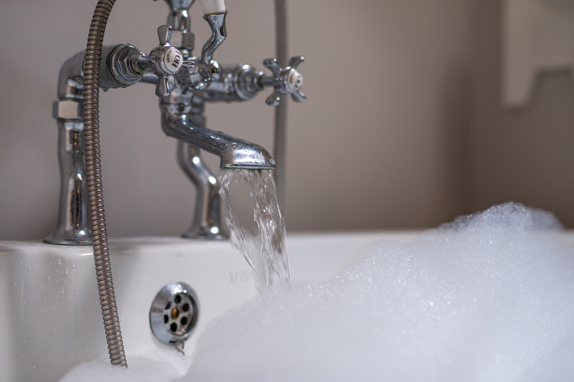 A close up of a bath tap running water into a bubble bath