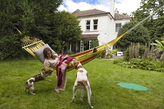 A lady in her garden on a hammock with her two dogs, in the background you can see a underground tank and her rural home