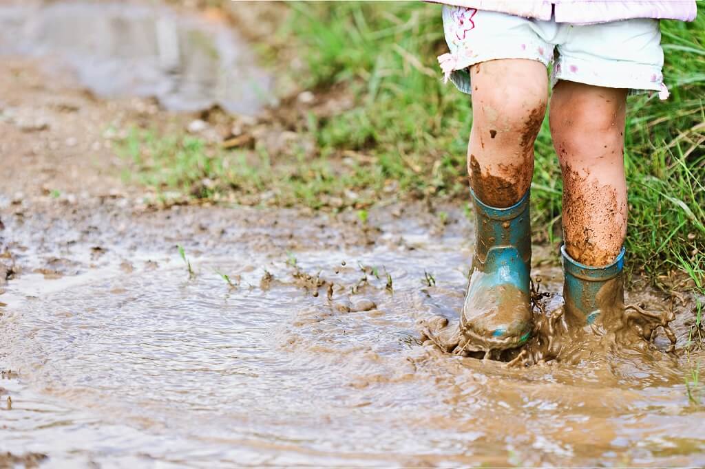 Small child splashing in muddy puddles wearing wellington boots
